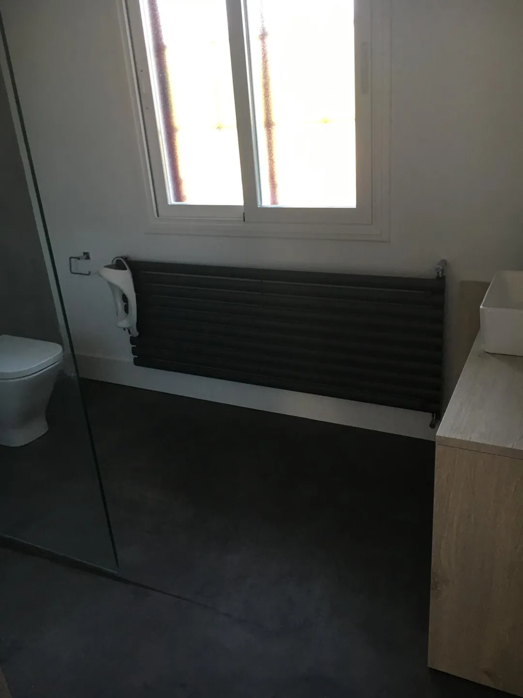 Baño con suelo oscuro, radiador toallero y mampara de vidrio