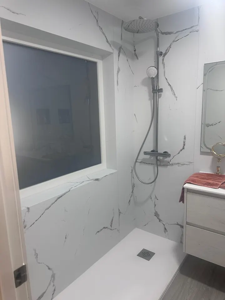 Baño reformado en mármol blanco con ducha a ras de suelo y ventana interior