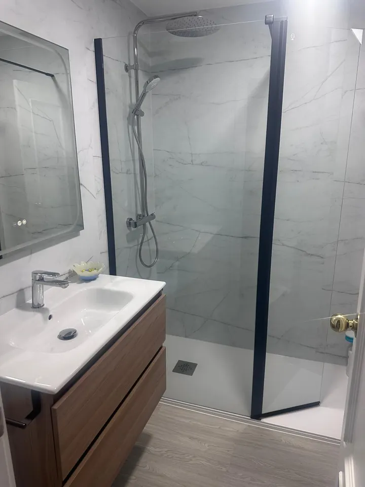 Baño reformado en mármol con mampara, mueble de madera y plato de ducha